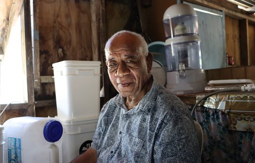 Moses, a community elder from Tonga, sits in his home next to his clean water tap.