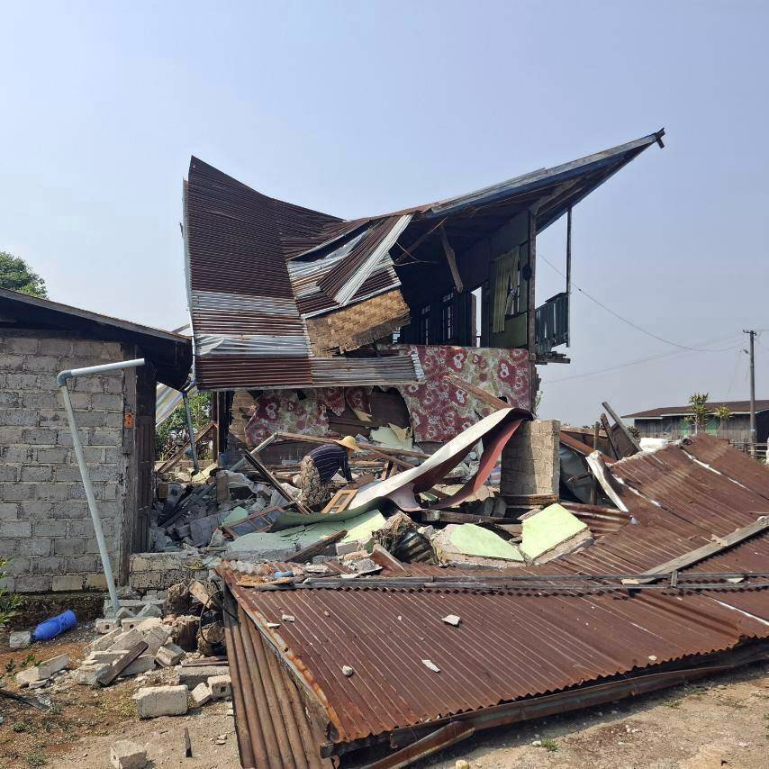 A woman in a wide brimmed hat searches through the rubble of a residential building