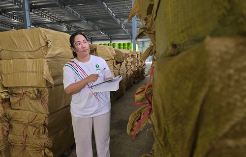 A woman in an Oxfam branded t-shirt stock-counts items on pallets in a warehouse.