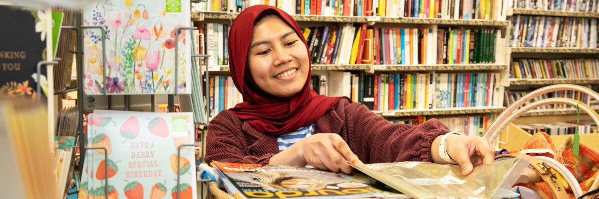 A smiling woman in a headscarf tidies a shelf.