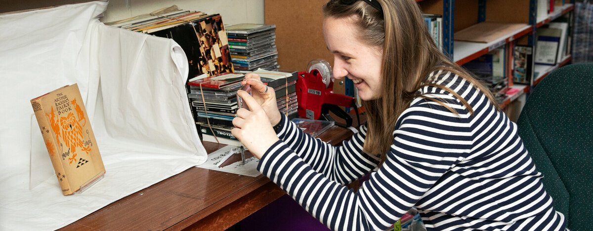 A woman smiling and taking a photograph of a book