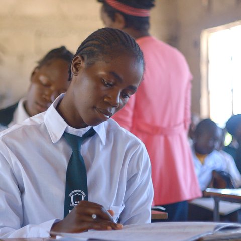 Children in white shirts with green ties in a classroom in Zimbabwe.
