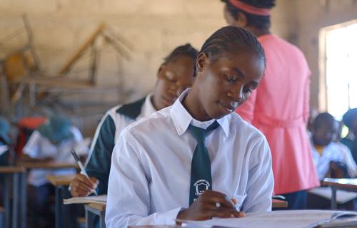 Children in white shirts with green ties in a classroom in Zimbabwe.