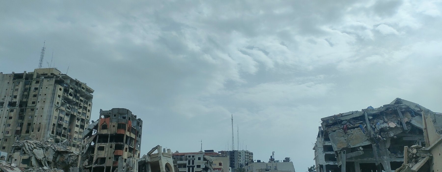 People walk in between destroyed buildings, turned to rubble