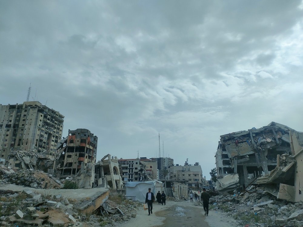 People walk in between destroyed buildings, turned to rubble