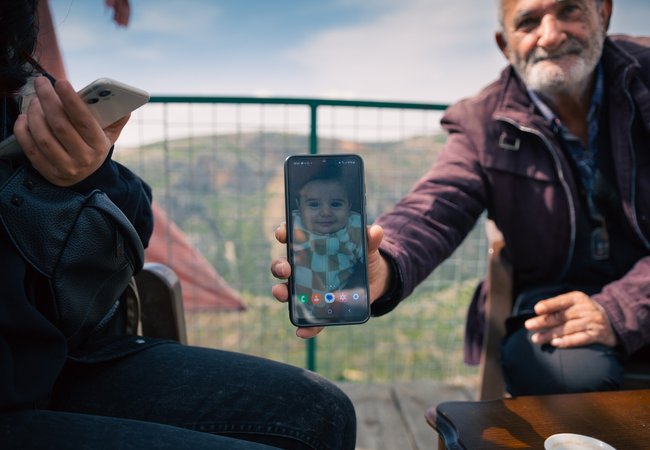 A proud grandfather holds up his phone showing a photo of his grandchild in Deir Mimas, Lebanon.