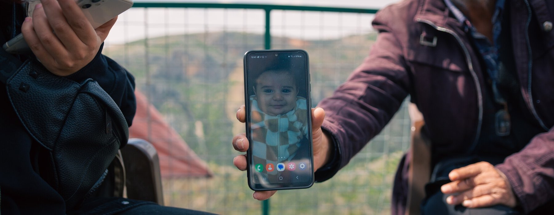 A proud grandfather holds up his phone showing a photo of his grandchild in Deir Mimas, Lebanon.