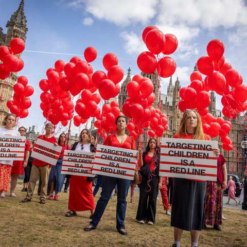 Campaigners dressed in red from Anti-Slavery International, Choose Love, Christian Aid, Doctors Without Borders/Médecins Sans Frontières, Oxfam and War Child UK stand holding 247 red helium balloons on the 25th of June 2025 in Westminster, London, United