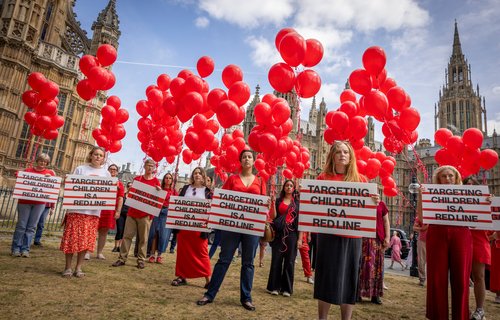 Campaigners dressed in red stand holding 247 red helium balloons on the 25th of June 2025 in Westminster, London, United