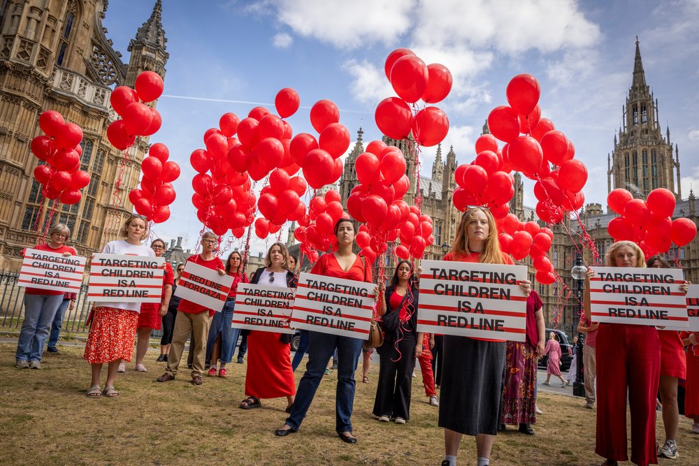 Campaigners dressed in red from Anti-Slavery International, Choose Love, Christian Aid, Doctors Without Borders/Médecins Sans Frontières, Oxfam and War Child UK stand holding 247 red helium balloons on the 25th of June 2025 in Westminster, London, United