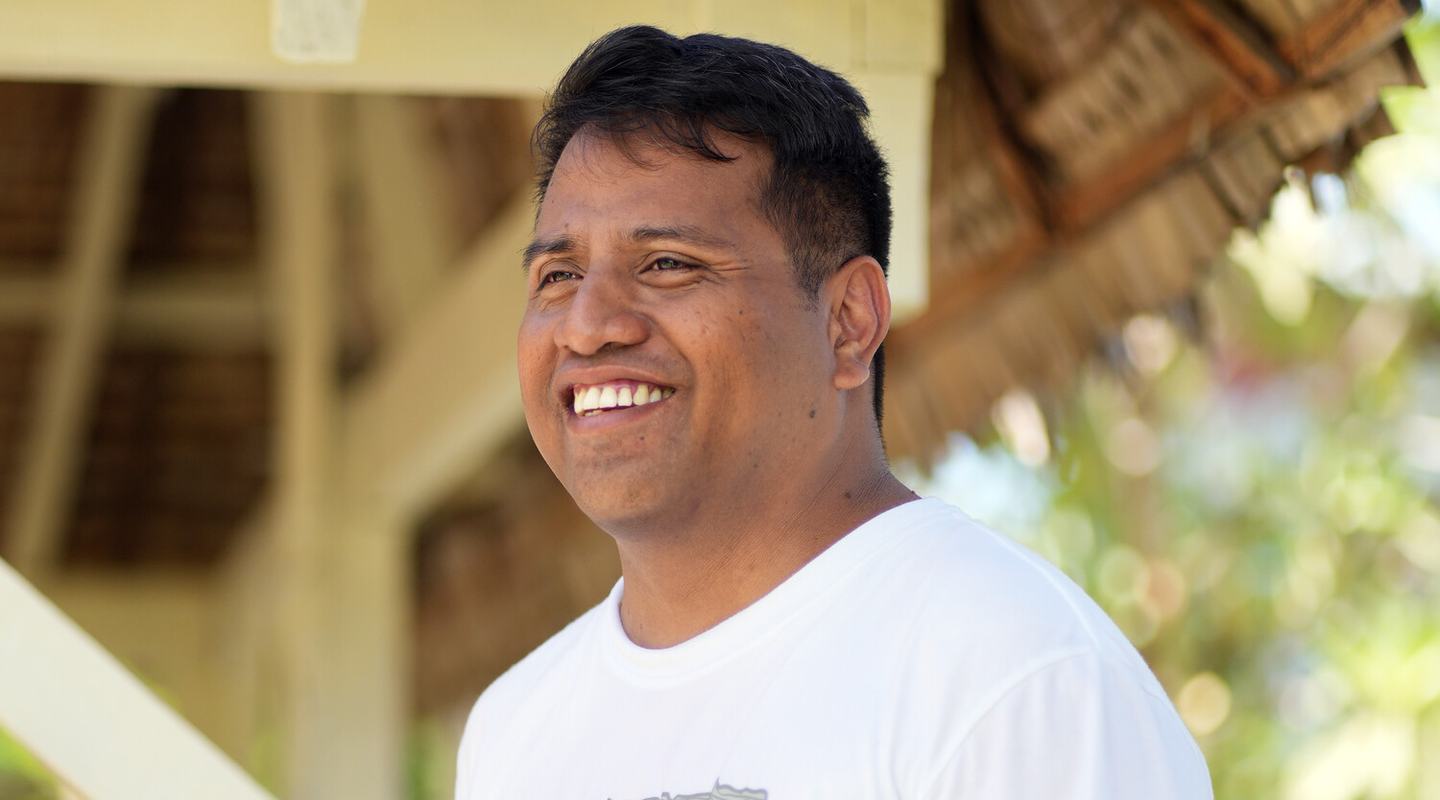 a man sitting outside, facing away from the camera and smiling.