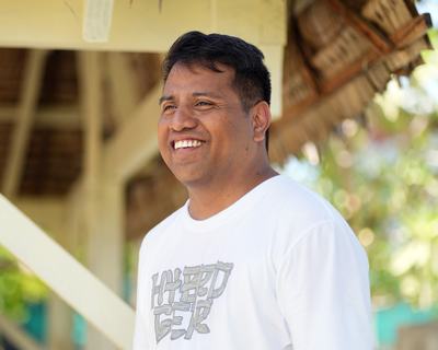 a man sitting outside, facing away from the camera and smiling.