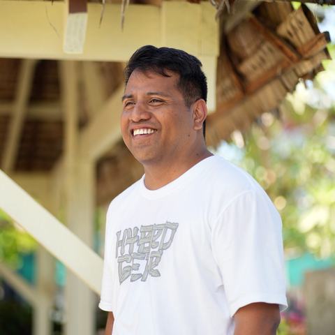 a man sitting outside, facing away from the camera and smiling.