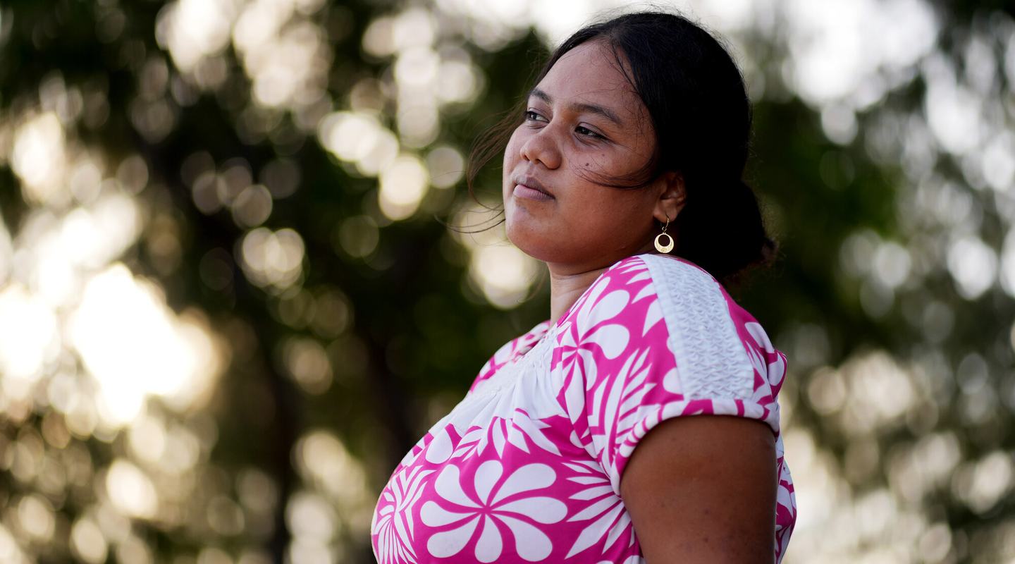 A woman looking into the distance, with greenery in the background.