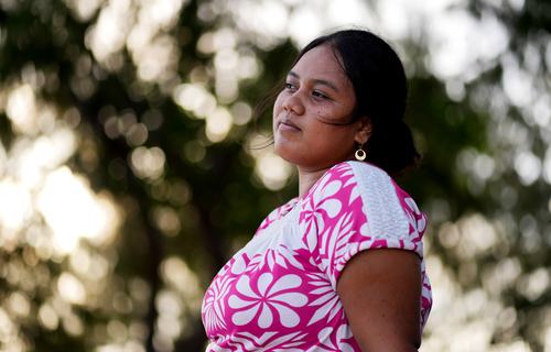 A woman looking into the distance, with greenery in the background.