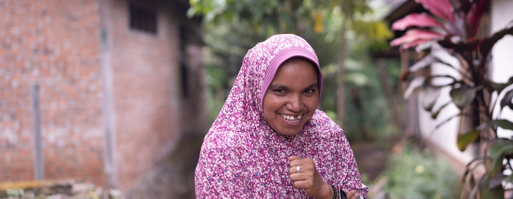 Salbia, a smiling woman with a pink head-scarf poses for a photo.