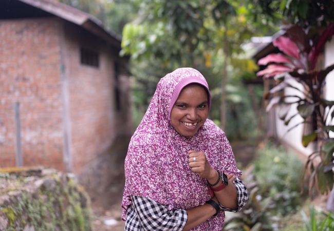 Salbia, a smiling woman with a pink head-scarf poses for a photo.