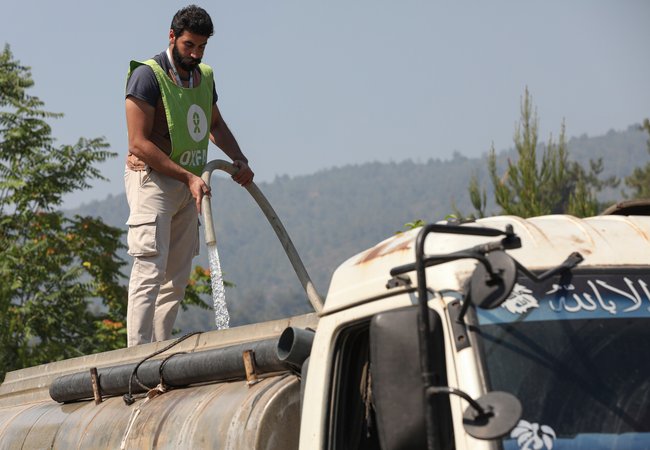 An Oxfam staff member refills a water tanker in Ballouran, rural Latakia, Syrian Arab Republic.