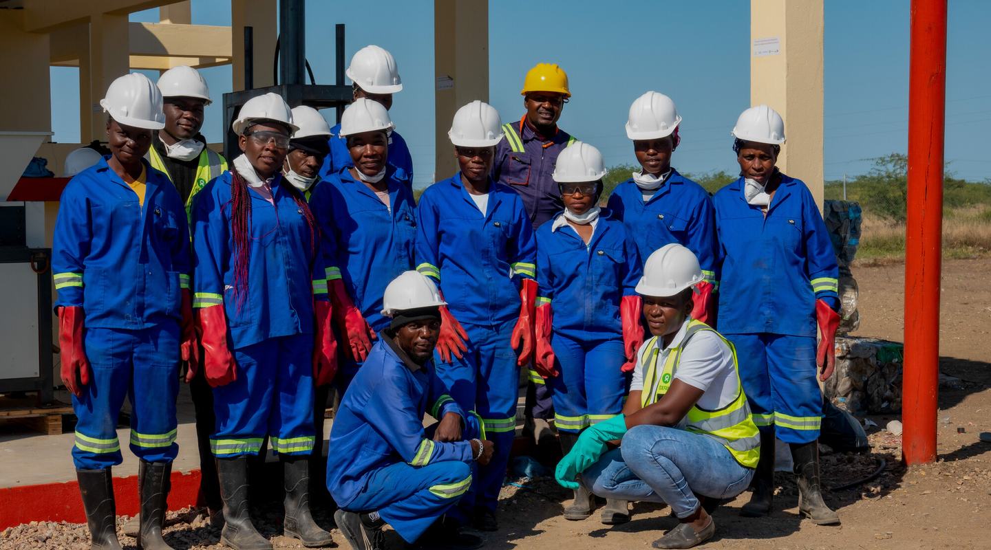 Members of the Waste Committee at Chokwe Waste Centre in Mozambique pose in blue overalls and white safety helmets.