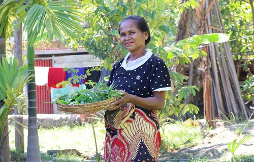 A smiling woman holds a basket containing her spinach crop in Timor-Leste