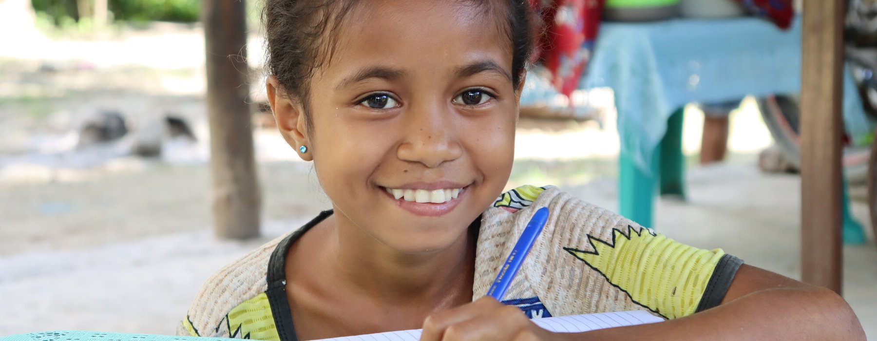 Auxiliadora (age 12) works on her writing in front of her home in rural Timor-Leste.