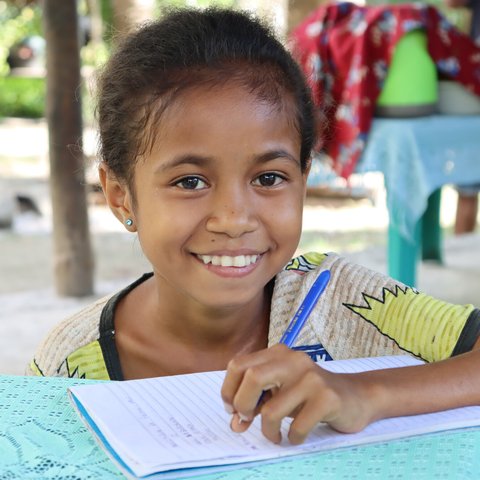 Auxiliadora (age 12) works on her writing in front of her home in rural Timor-Leste.