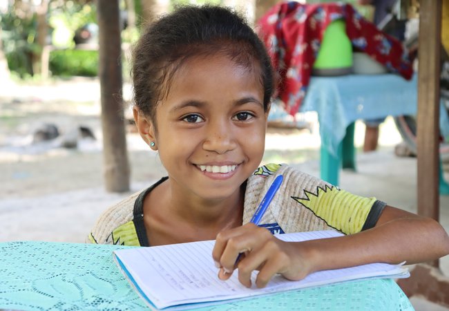 Auxiliadora (age 12) works on her writing in front of her home in rural Timor-Leste.