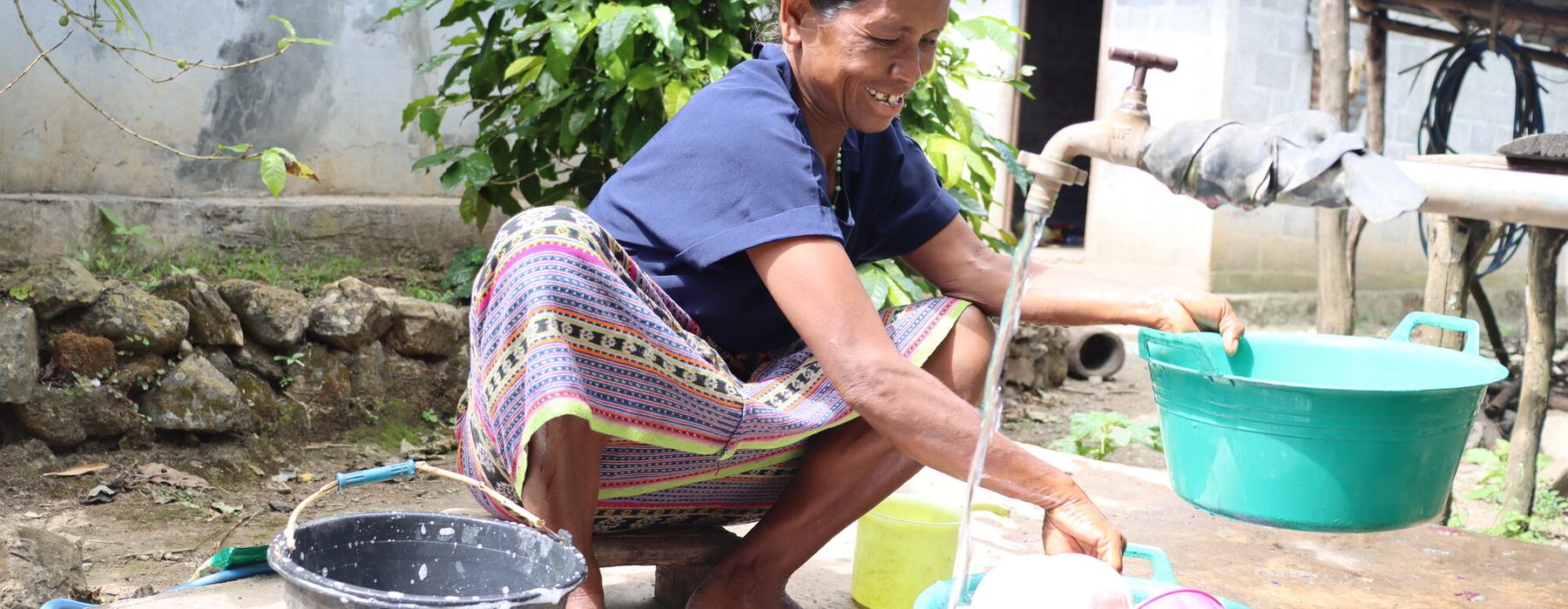 A woman to washes dishes outside her home in rural Timor-Leste with water from an Oxfam-supplied water tank.