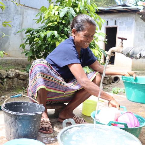 A woman to washes dishes outside her home in rural Timor-Leste with water from an Oxfam-supplied water tank.