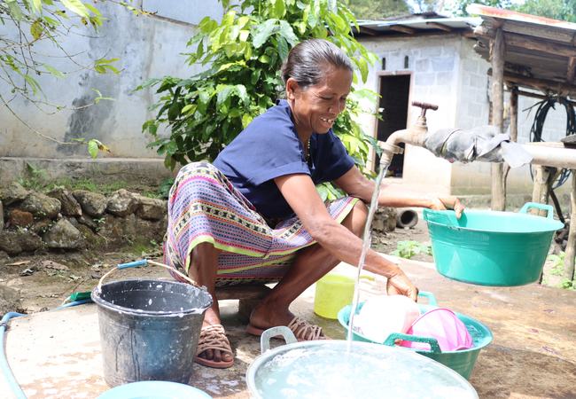 A woman to washes dishes outside her home in rural Timor-Leste with water from an Oxfam-supplied water tank.