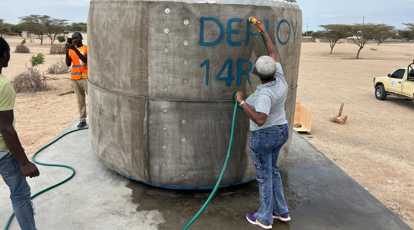 A woman using a hose to spray an inflatable tank with water.