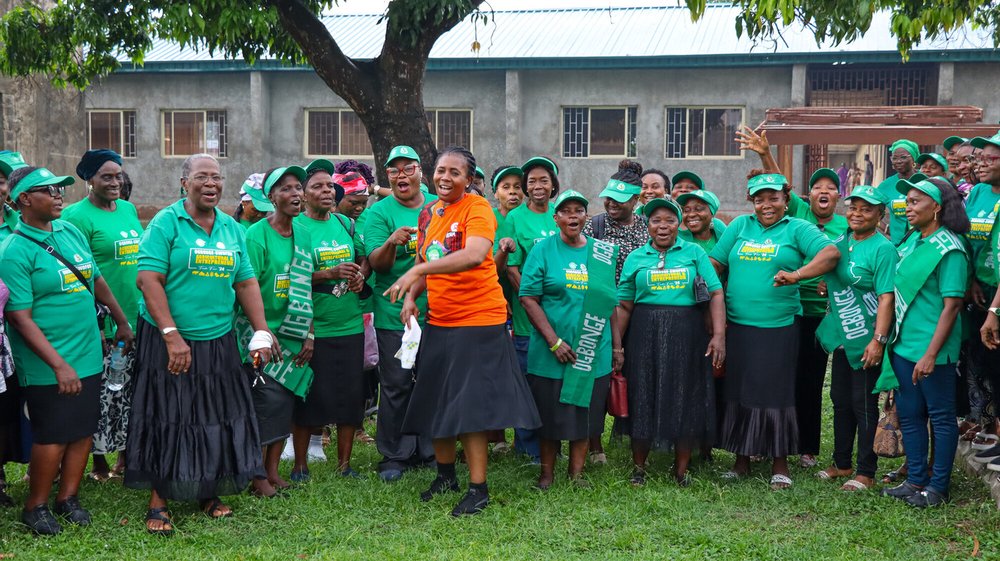 A large group of Ogbonge women wearing bright green t-shirts smiling and singing together
