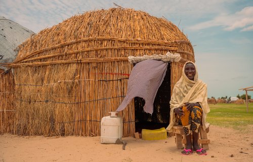 a woman sat outside a hut, smiling.