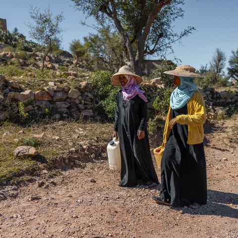 Abeer and her sister are walking along a dusty track carrying empty water containers in a district of Taiz, Yemen.