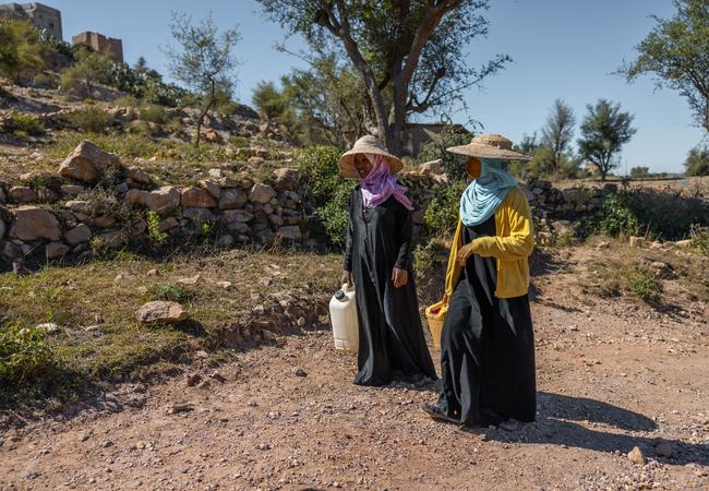 Abeer and her sister are walking along a dusty track carrying empty water containers in a district of Taiz, Yemen.