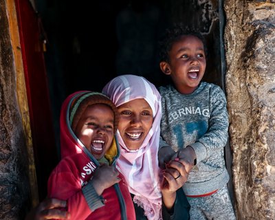 A woman and two children hold hands and smile in the doorway of their home in Taiz, Yemen, as the sun shines on them.