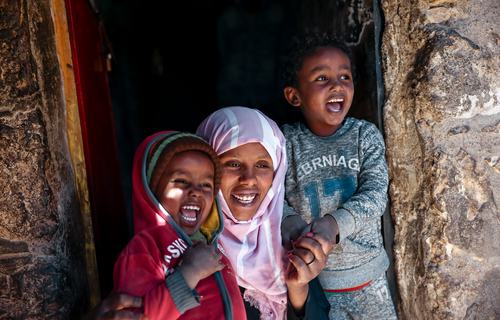A smiling woman and her two young children outside their home in Yemen.