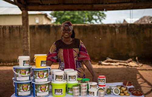 Safura is standing at her stall with a table full of the shea products she has produced with the Bunglung women's co-operative including large containers down to small tins.