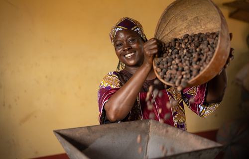 Safura smiles as she tips a basket of shea nuts into a processing machine.