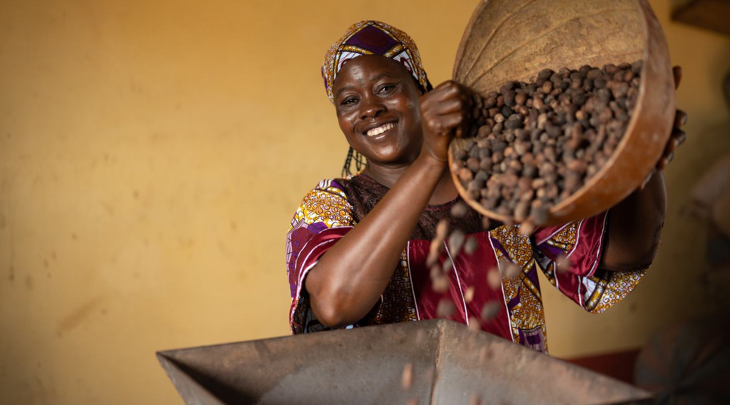 Safura smiles as she tips a basket of shea nuts into a processing machine.