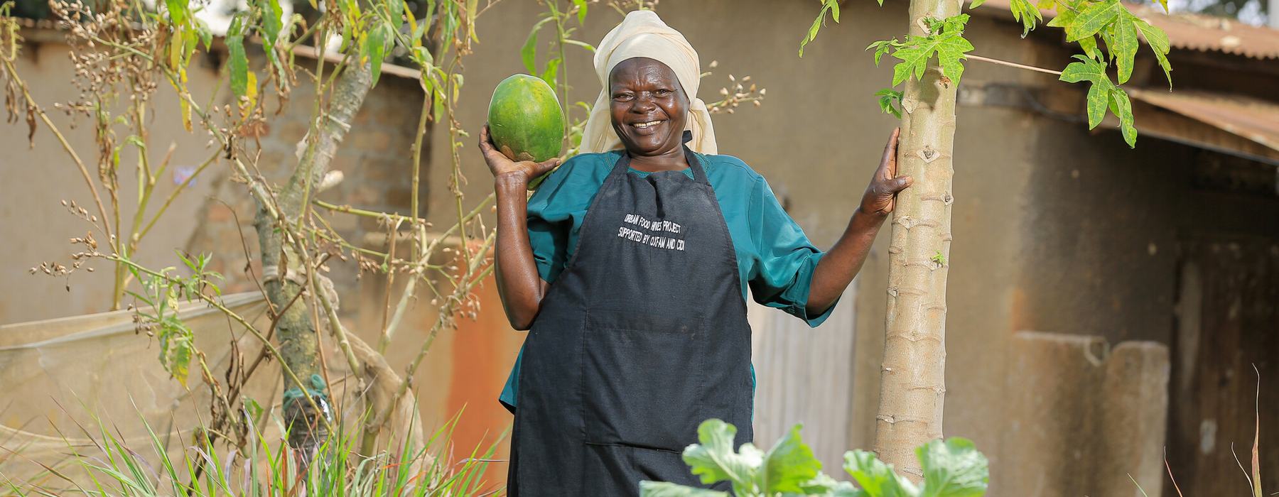 A smiling woman holds up a green melon in her vertical garden in Uganda