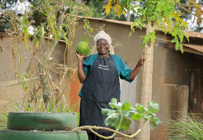 A smiling woman holds up a green melon in her vertical garden in Uganda