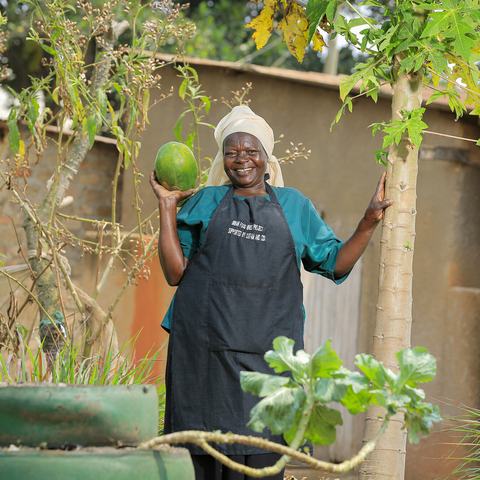 A smiling woman holds up a green melon in her vertical garden in Uganda