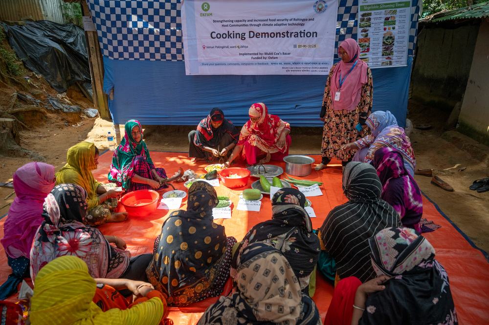 A group of women are sat on a large orange rug with bowls and sheets of paper participating in a practical cooking demonstration.