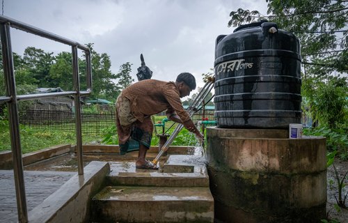 Rafiq is bending over to use a tubewell tapstand installed in Cox's Bazar