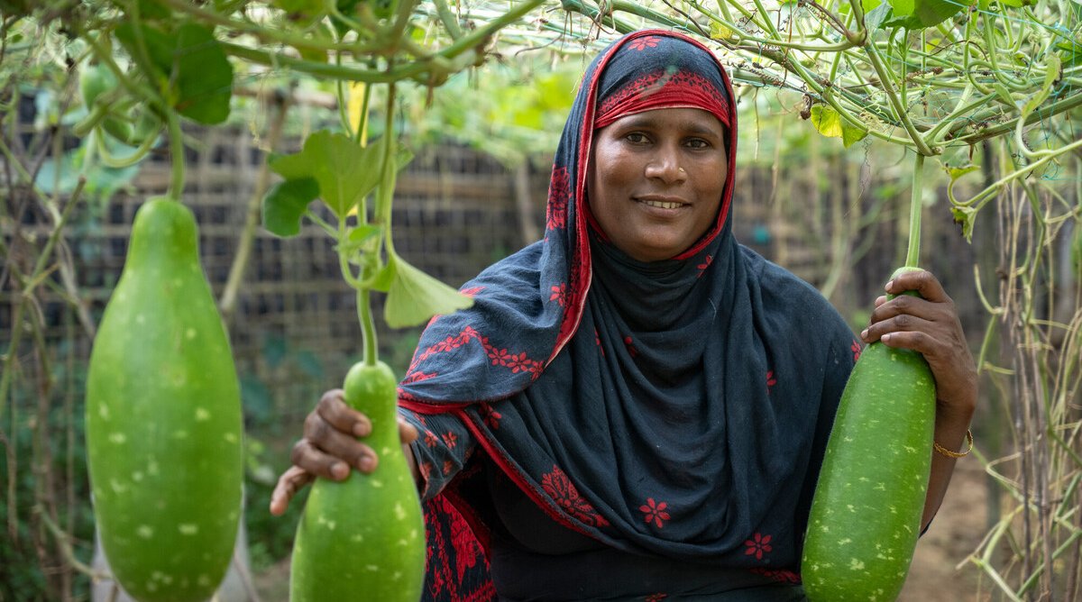 Aysha in her homestead garden holding the gourds she has grown herself