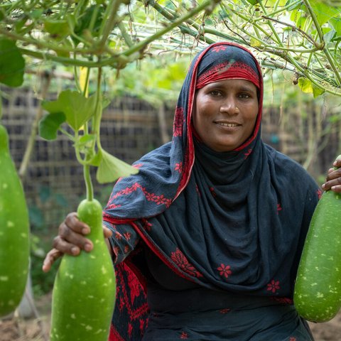 Aysha in her homestead garden holding the gourds she has grown herself