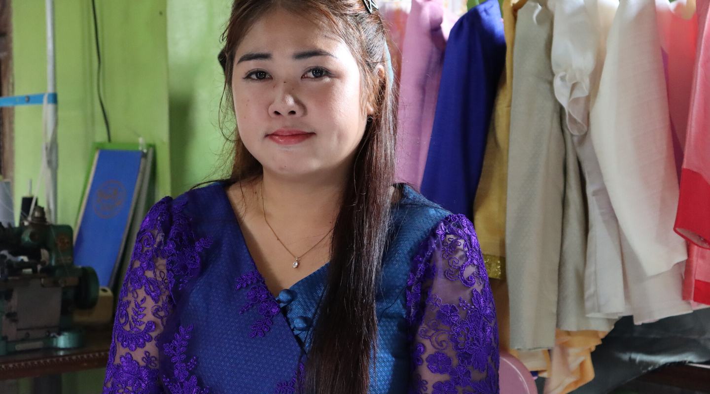 a woman sat in front of a colourful selection of hanging clothes.