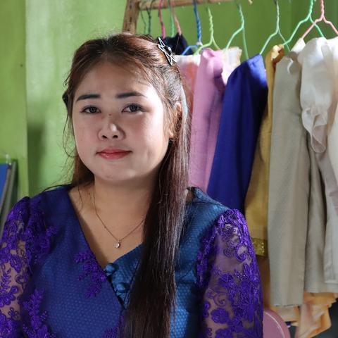 a woman sat in front of a colourful selection of hanging clothes.