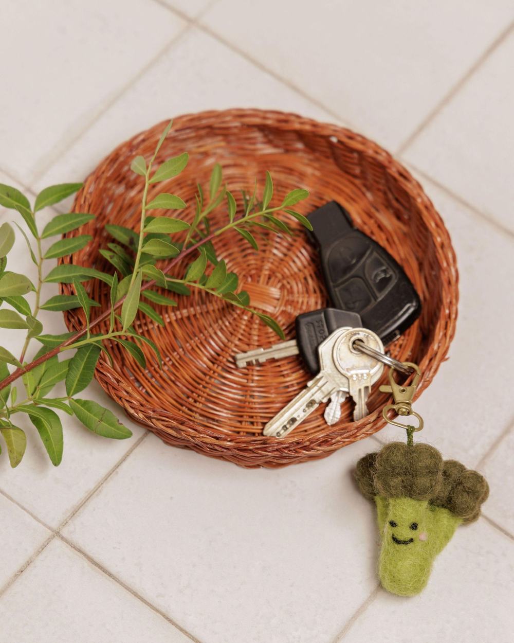 A broccoli smiley felt keyring pictured next to a wicker tray and car keys